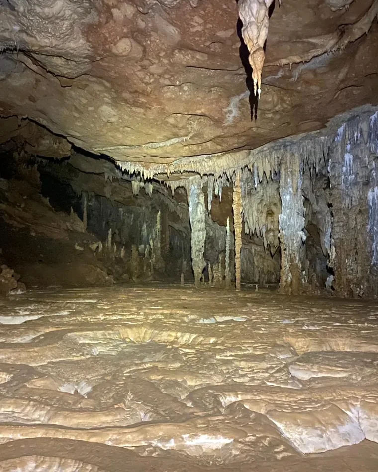Dark limestone chamber with stalactites and a wet cave floor in Belize